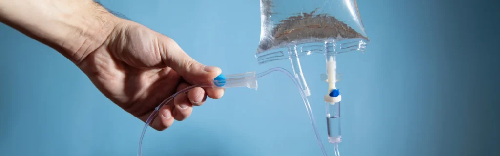 Close-up of a hand holding IV tubing connected to an intravenous infusion bag